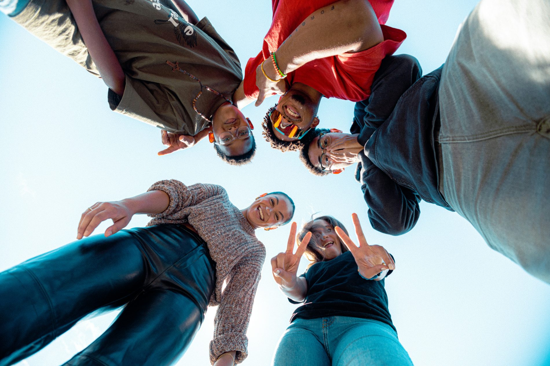 A group of teens in a circle making peace signs, seen from below against a blue sky